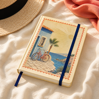 Carnet LABON personnalisé style méditerranéen, couverture rigide crème, bordure estampillée, vélo rouge vintage, scène côtière, feuille d'or, soleil, ruban bleu marine