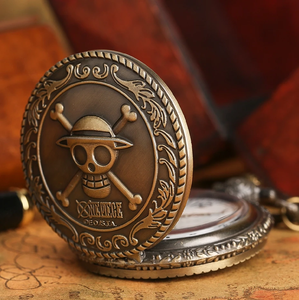 Reloj de bolsillo de una pieza de latón vintage, Con el icónico cráneo pirata de sombrero de paja y emblema de tibias cruzadas en su tapa detallada. - Product Image 1
