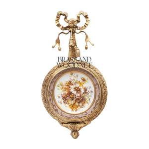 Art mural en laiton antique avec cadre orné de ruban et pièce maîtresse en porcelaine florale dans un style vintage élégant - Product Image 1