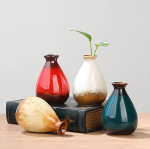 Un conjunto de cuatro jarrones de cerámica coloridos y de forma única, con tres en posición vertical, dispuestos en una pila de libros antiguos. - Product Image 1