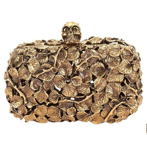 An elegant gold-toned clutch covered in a detailed gingko leaf pattern with a striking skull clasp. Available at wholesale price - Product Image 1