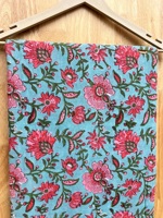 Kain katun murni premium dengan motif bunga berwarna merah muda cerah, pola bunga merambat yang indah dicetak di atas kain berwarna biru kehijauan lembut.