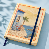 Carnet LABON personnalisé style méditerranéen, couverture rigide crème, bordure estampillée, vélo rouge vintage, scène côtière, feuille d'or, soleil, ruban bleu marine