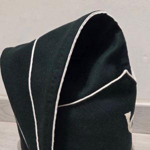 Ceci est un chapeau bicorne en feutre de laine vert foncé avec une bordure blanche et un pompon décoratif, doté d'un emblème de corne de cheval. - Product Image 3