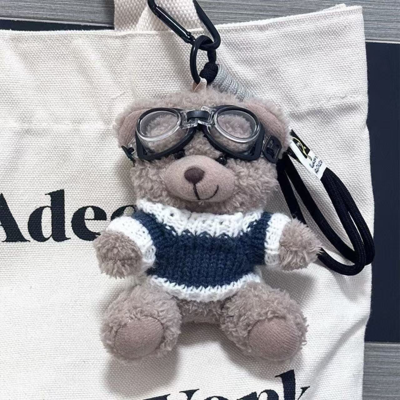 Un ours brun avec des lunettes, des vêtements bleus et un cordon noir.