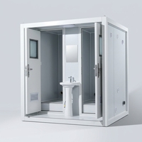 Cabine de toilette préfabriquée à deux compartiments avec portes en acier ouvertes et lavabo partagé