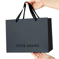 Sac shopping personnalisé en papier métallisé argenté avec logo noir et larges poignées en ruban de satin noir pour vêtements de luxe