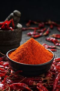 Poudre de piment rouge dans un bol en argile avec des piments séchés à côté - Product Image 4