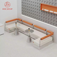 Ensemble de mobilier de restaurant commercial, canapé en cuir blanc en forme de L, tables rondes en métal, chaises orange pour la restauration et l'hôtellerie