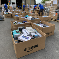 Palette de retours de produits électroniques variés de la boîte mystère Amazon : smartphones, ordinateurs, projecteurs, écouteurs et bagues connectées