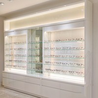Système d'affichage mural pour lunettes en laque blanche avec étagères LED lumineuses et comptoir à tiroirs pour l'aménagement de magasins d'optique