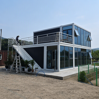 Conteneur Détachable à Double Étage avec Façade Modulaire en Verre, Terrasse Ouverte et Escalier Extérieur en Métal pour Utilisation en Camping en Milieu Rural ou sur Colline