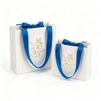 Sac en papier personnalisé avec emblème floral mat ivoire estampé à chaud or, avec poignée en ruban de satin bleu, pour cadeaux cosmétiques