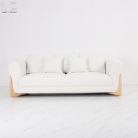 Canapé d'intérieur moderne avec accoudoirs arrondis rembourrés en blanc, pieds décoratifs en bois et coussins décoratifs pour salon