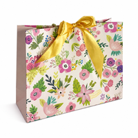 Sac cadeau en papier imprimé floral avec nœud en satin doré et poignées en corde torsadée pour l'emballage de cadeaux de détail