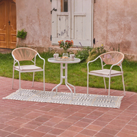 Ensemble bistrot 3 pièces aspect rotin, table ronde avec plateau en verre et 2 chaises à accoudoirs tressés avec coussin, cadre blanc, ensemble de jardin extérieur