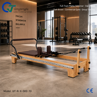 Reformer de Pilates pleine longueur en bois de chêne brun foncé avec barre de repose-pieds spécialisée pour les salles de sport commerciales et les salles d'entraînement en groupe