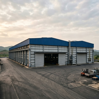 Bâtiment industriel préfabriqué à grande portée en structure acier, avec panneaux gris-bleu et fenêtres latérales longues, pour usine rurale