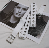Cette ceinture en toile tissée entièrement blanche, au style audacieux, avec boucle à plaque et œillets métalliques argentés sur toute la longueur, offre une ambiance cool et punk pour le streetwear.