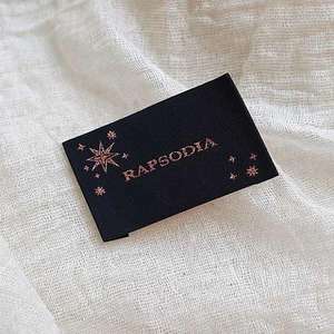 Etiquetas textiles tejidas para ropa con logotipo personalizado, tipografía, detalles de talla e instrucciones de cuidado de la prenda. - Product Image 1