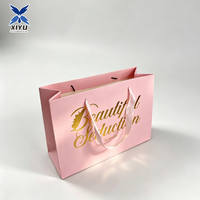 Sac cadeau en papier rose clair avec poignée en ruban de satin et impression dorée, élégant sac de transport pour boutique, produits de beauté, vente au détail et événements.