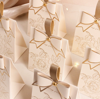Nouvelle boîte à bonbons de mariage blanc crème avec un design rétro de style français, dotée d'un nœud couleur champagne et d'une texture élégante.
