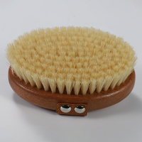 Cepillo exfoliante ovalado de madera de acacia con cerdas de jabalí, correa de mano de lona blanca y remaches plateados para un agarre seguro en superficies húmedas.