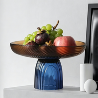 Twee-kleurige glazen fruitschaal, amberkleurige plaat met blauwe geribbelde voet, moderne decoratieve serveerschaal op voet voor thuis op tafel.