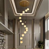 Lustre moderne en spirale pour escalier long, avec boules en albâtre naturel et structure métallique, idéal pour villa et hall à plafond haut