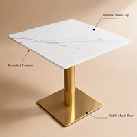 Table et chaises de restaurant, plateau carré en pierre frittée avec base cylindrique dorée et fauteuils beiges à accoudoirs en forme de baril pour café-bar