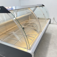 Vitrine réfrigérée moderne en verre incurvé pour la présentation de fromages artisanaux dans les sections de charcuterie des magasins spécialisés en produits alimentaires.