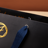 Sac en papier noir avec logo imprimé personnalisé, avec œillets métalliques renforcés et poignées en ruban pour l'emballage de produits cosmétiques et de soins de la peau