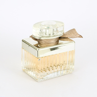 Perfume Femenino en Envase Rectangular de Vidrio con Franjas Plateadas, Lazo de Cinta Marrón, Tapa Dorada y Caja Dorada. Aroma Atemporal para Aniversario.
