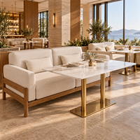Ensemble de canapés de restaurant de style côtier moderne, chaises et tables, canapé en chêne clair avec coussins crème et table en marbre blanc avec pieds dorés