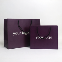 Sac en papier teinté violet foncé avec poignées en corde tressée noire, soufflet et impression de logo blanc personnalisé pour marques de cosmétiques