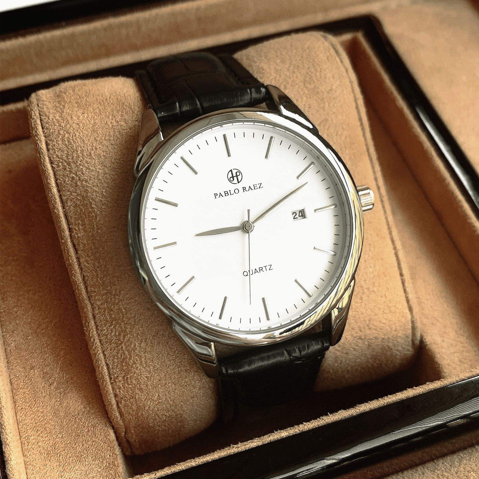 Carcasa plateada, correa negra, esfera blanca.