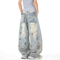 Jean vintage délavé coupe large avec broderie abstraite, œillets métalliques, effet usé et bords effilochés, style streetwear ample