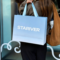 Sac cadeau en papier bleu poussière mat avec ruban en satin blanc et poignée à nœud, logo personnalisé en serif, sac de luxe pour boutique de parfums