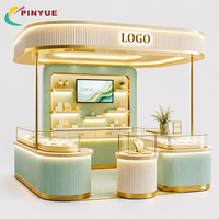 Kiosque de présentation de bijoux vert sauge et or avec panneaux cannelés, éclairage LED et comptoirs vitrine arqués pour stands de boutiques en centre commercial
