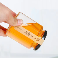 Stoples Madu Kaca Soda-Lime Heksagonal Mewah dengan Tutup Logam Hitam. Gaya Modern. Logo Kustom. Cetak Cap Emas Sistem Sablon.