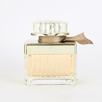 Perfume Femenino en Envase Rectangular de Vidrio con Franjas Plateadas, Lazo de Cinta Marrón, Tapa Dorada y Caja Dorada. Aroma Atemporal para Aniversario.