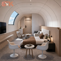 Capsule habitable avec chambre, salon, salle de bain, fenêtre incurvée en verre, lucarne, coque blanche, cadre foncé, maison capsule préfabriquée