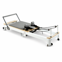 Reformer Pilates avec cadre en bois et coussinets gris pour l'entraînement et les étirements du tronc en studio