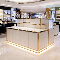 Comptoir de présentation de cosmétiques et de parfums de luxe hors taxes avec panneaux blanc crème, lignes de finition dorées et éclairage LED pour aménagement de magasin de détail