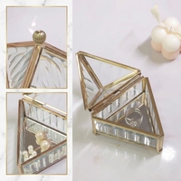 Boîte à bijoux triangulaire en verre avec cadre métallique doré, couvercle pyramidal et chaîne pour le rangement et la présentation de bijoux et de bagues
