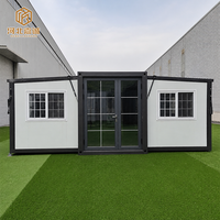 Maison préfabriquée portable à double aile extensible avec panneaux extérieurs foncés, structure blanche et plan d'aménagement ouvert pour une habitation temporaire