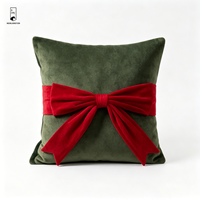 Coussin carré décoratif en velours vert foncé avec nœud rouge, idéal pour les fêtes de Noël et l'ambiance festive à la maison