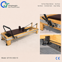 Reformer de Pilates pleine longueur en bois de chêne brun foncé avec barre de repose-pieds spécialisée pour les salles de sport commerciales et les salles d'entraînement en groupe