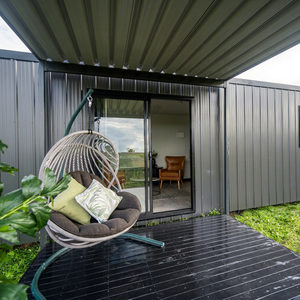 Maison préfabriquée minimaliste en conteneur avec porte coulissante en verre, cadre en alliage d'aluminium, cabane modulaire extérieure avec fauteuil suspendu et terrasse - Product Image 1