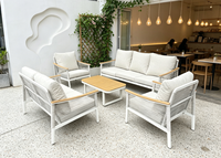Ensemble de salon d'extérieur moderne en métal blanc, sièges à texture tressée, tables rondes avec accents en bois et coussins gris moelleux, idéal pour le patio
